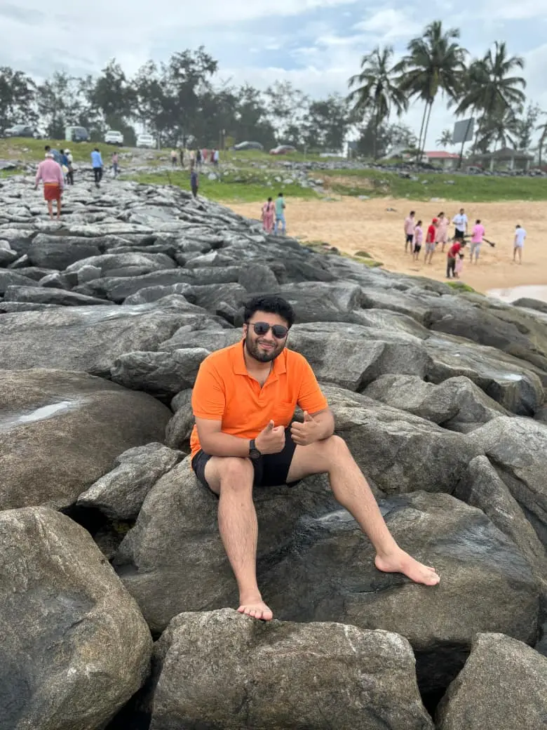 Raghavendra sitting barefoot on sea rocks giving two thumbs up